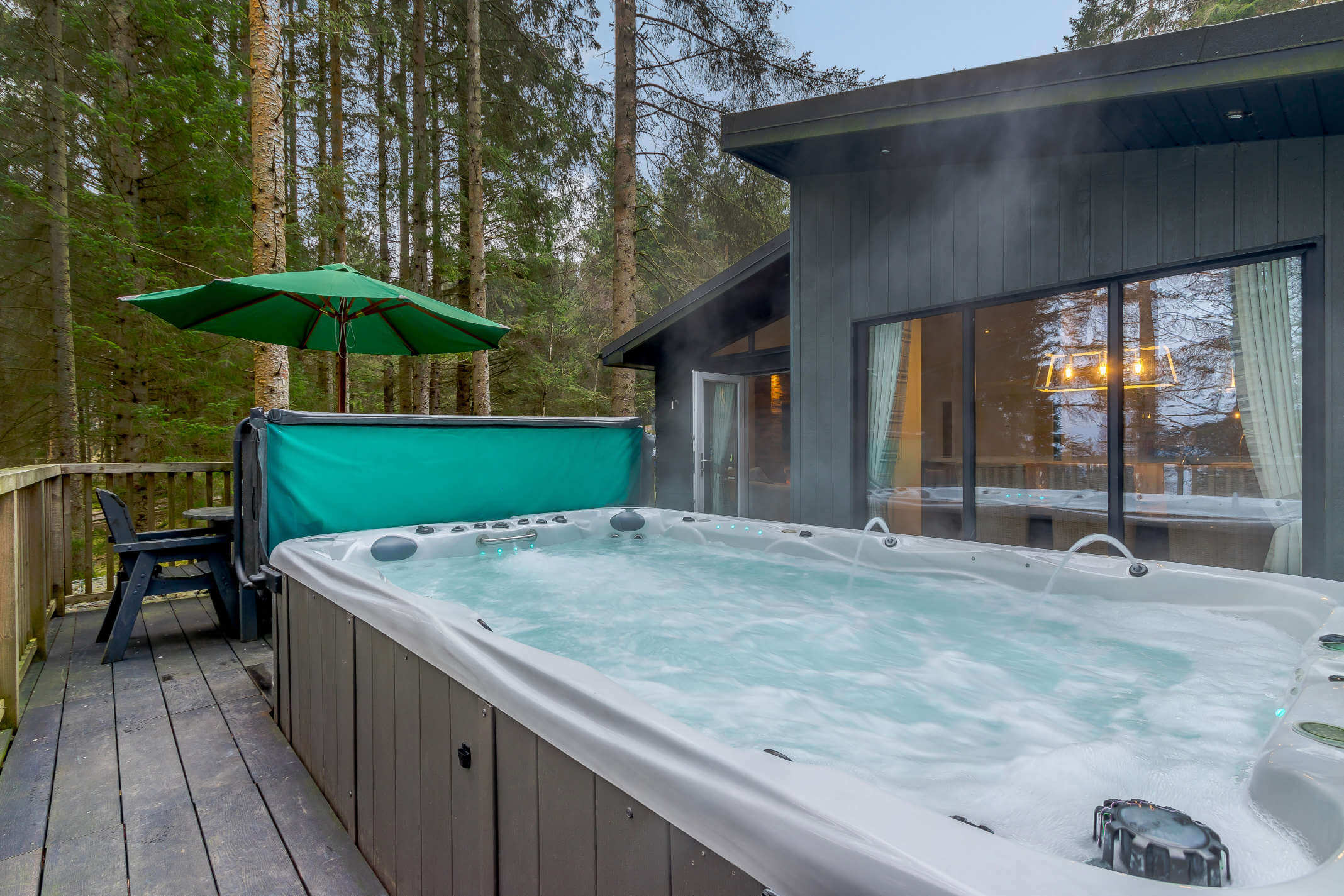 Hot tub lodge at Kielder Waterside. The hot tub is bubbling away on the decking surrounded by the forest.