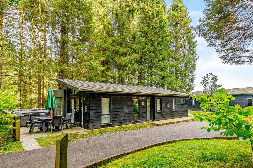 Beech Premier Spa at Kielder Waterside. A view of the single story luxury lodge and hot tub patio.