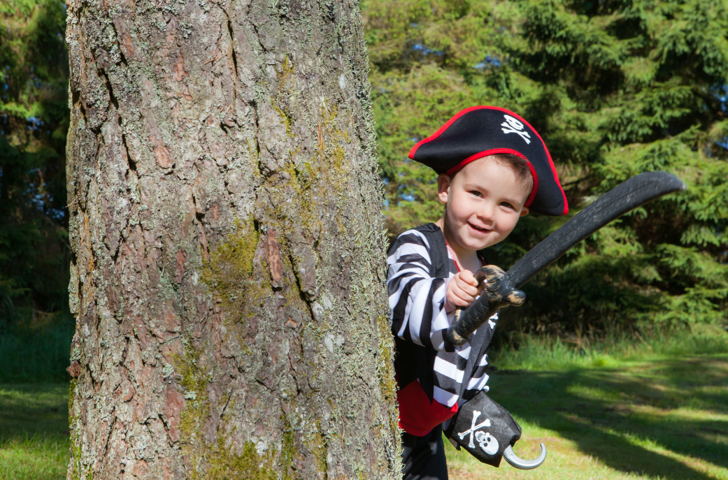 Pirates on the Ferry at Kielder Waterside. Child peering around side of tree in pirate costume