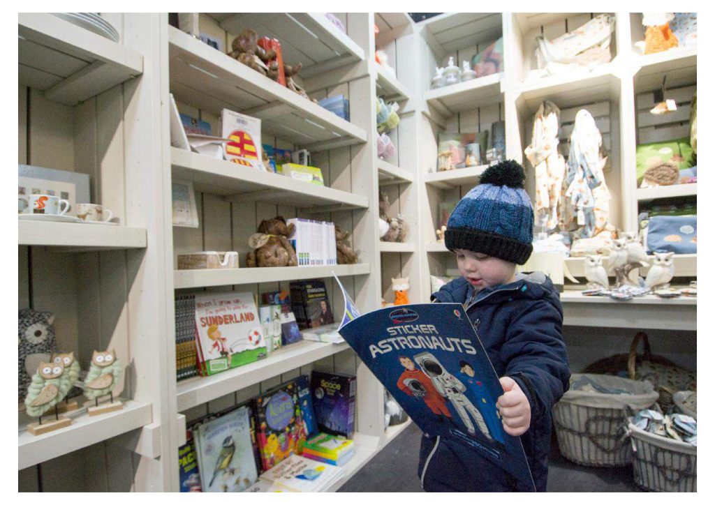 Young boy reading a book about space whilst stood in the Kielder Waterside Shop